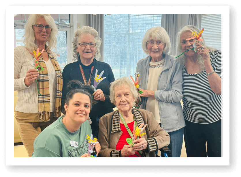 Elderly Women Showing Completed Craft Projects with Staff at Assisted Living Facility