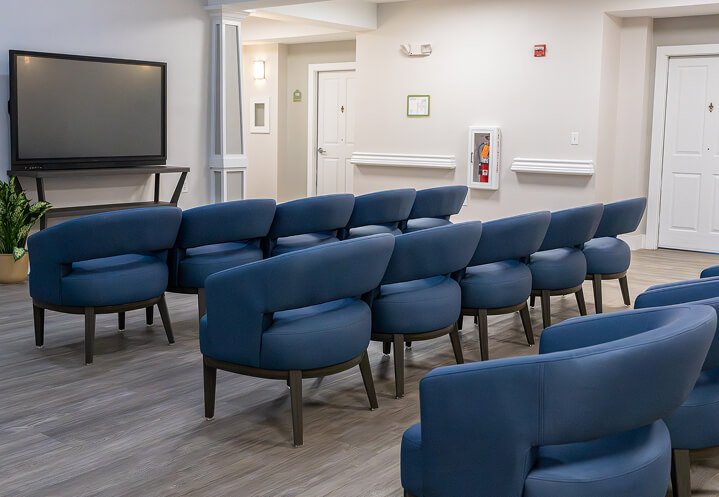 TV Lounge with Modern White Seating and Ceiling Fan at Assisted Living Facility Movie Theater Room For Seniors Living in Memory Care Facility