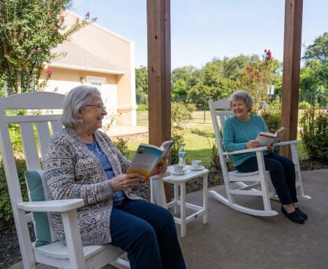 Two Elderly Women Reading Books on Outdoor Patio at Assisted Living Facility Two Elderly Women Reading Books on Outdoor Patio at Assisted Living Facility