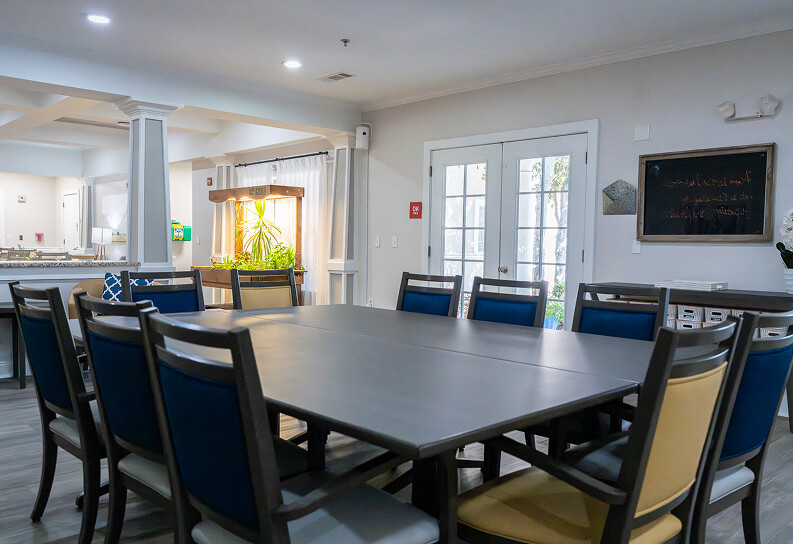 Sitting Room with Fireplace and Floral Accent Chairs at Assisted Living Facility Open Space Lounge Area with Table and Chairs For Seniors in Memory Care Facility